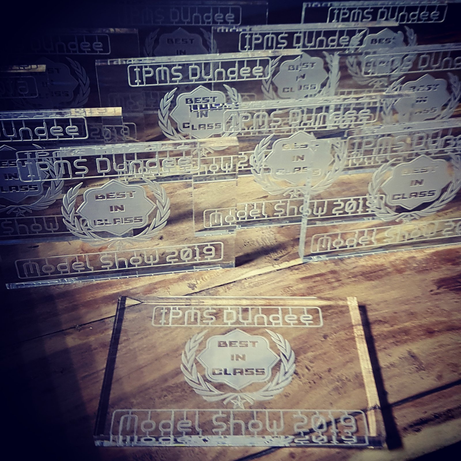 Laser engraved acrylic awards for IPMS Dundee Model Show arranged on a wooden workbench